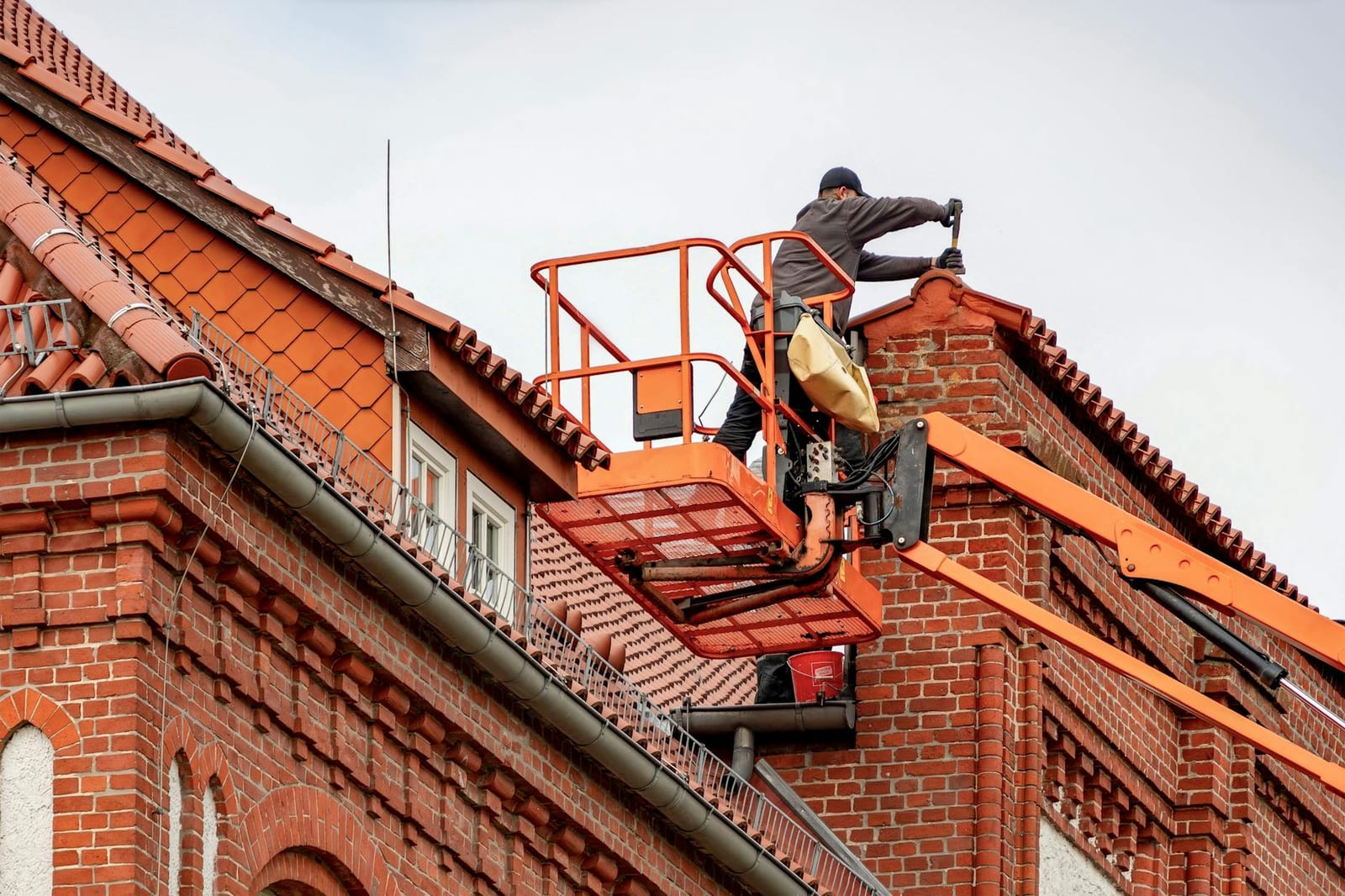 Roofer on a lift performing gutter and roof repair on a brick home